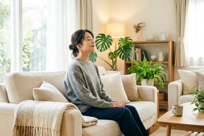 明るいリビングでソファに座り、目を閉じて深呼吸をしているリラックスした表情の女性