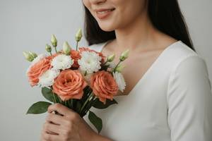 花束を持って微笑む女性の手元のクローズアップ。画像内にテキスト・文字・ロゴ・記号・数字・ラベルは一切含めないこと。