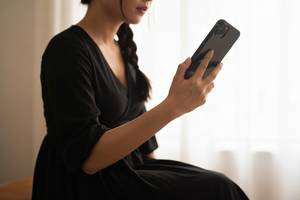 スマートフォンを斜め上に構えて自撮りの角度を調整している手元のクローズアップ。画像内にテキスト・文字・ロゴ・記号・数字・ラベルは一切含めないこと。