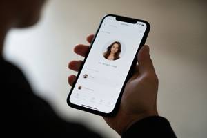 スマートフォンを持つ手と、画面に映るマッチングアプリ風のプロフィール画面のぼかしたイメージ。画像内にテキスト・文字・ロゴ・記号・数字・ラベルは一切含めないこと。