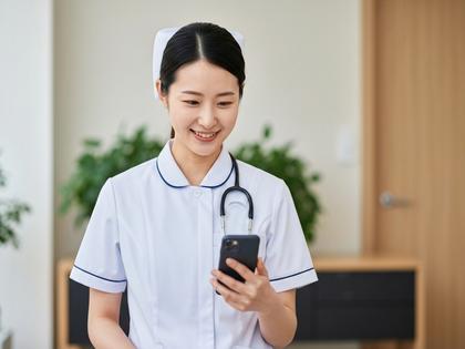 スマホを見ながら微笑む白衣の看護師女性