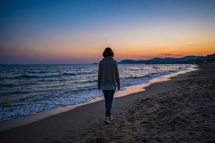 夕暮れの海辺をひとりで歩く女性の後ろ姿