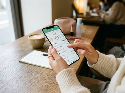 カフェでスマホの家計簿アプリを使う手元。