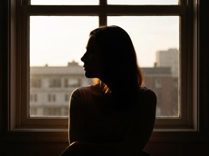 窓辺で考え込む女性の後ろ姿、柔らかい自然光