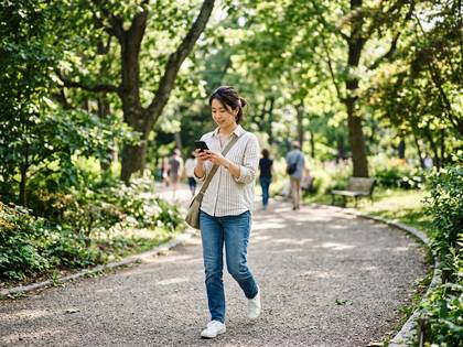 公園でスマホを見ながら歩く女性。