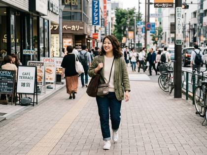 日本の商店街の舗道を笑顔で歩く女性。