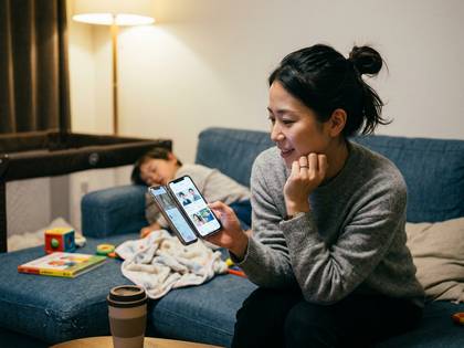 ソファでくつろぎながらスマホを見る女性と、隣で眠る子供。