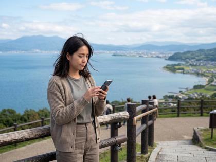 琵琶湖を背景にスマートフォンを見つめる若い女性のイメージ