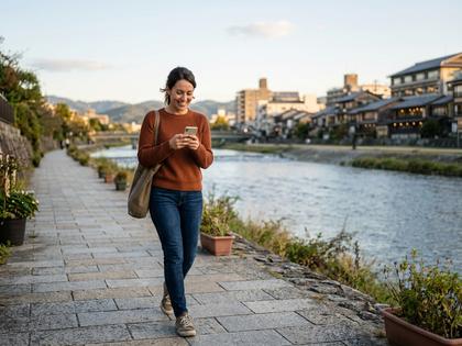 京都の鴨川沿いを歩く女性がスマホを見て微笑んでいる様子
