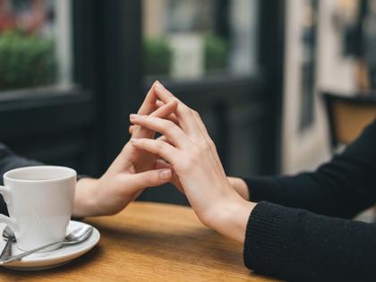 カフェのテーブル越しに手を伸ばし指を絡める女性の手元