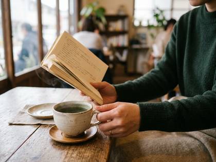 カフェで温かいお茶と本を楽しむ緑のセーターの女性。