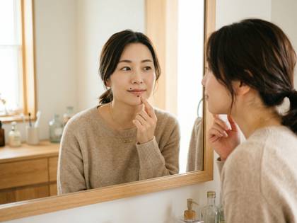 鏡に映る自分を見つめ、口元を触って確認する女性。