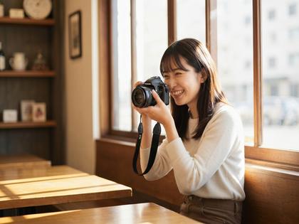 自然光の入るカフェで笑顔の女性が撮影しているイメージ