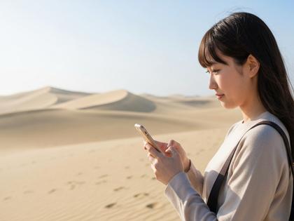 鳥取砂丘を背景にスマホを操作する20代女性のイメージ
