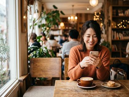 カフェでスマホを見ながら笑顔の30代女性