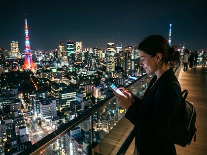 東京の夜景を背景にスマホを操作する女性のイメージ