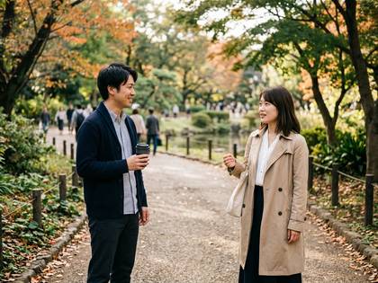 秋の公園でコーヒーを片手に笑顔で会話する男女。