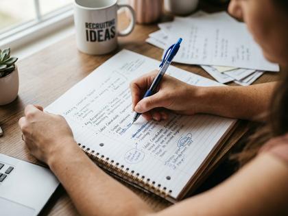 ノートに募集文の下書きをする女性の手元