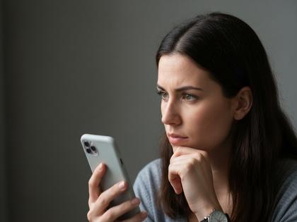 スマホ画面を見ながら考えごとをする女性のイメージ