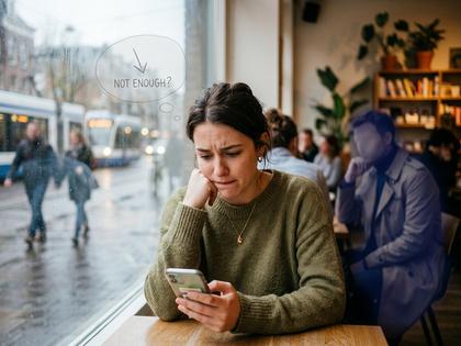 カフェの窓辺でスマホを見つめながら少し不安そうな表情を浮かべる20代女性