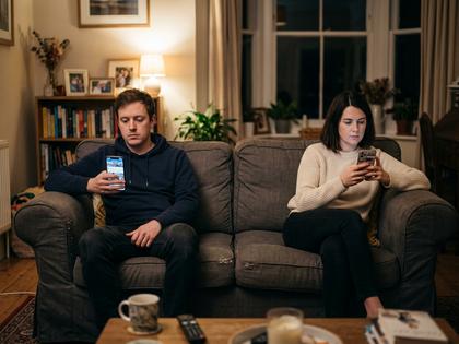 部屋でそれぞれスマホを見ながら並んで座るカップル