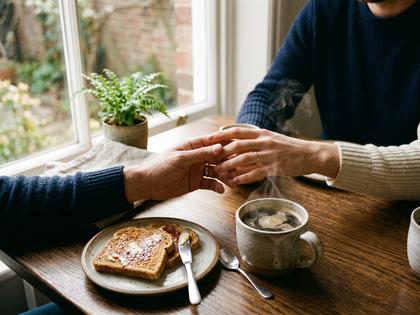 朝の食卓で向かい合い、コーヒーを置く夫婦の手元 800×600