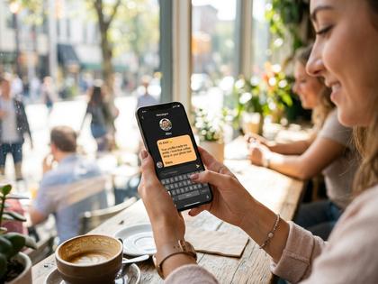 スマートフォンでメッセージ画面を開き、やわらかく微笑む20代後半の女性。明るいカフェの窓際、800px×600px